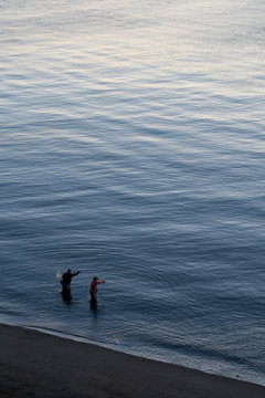 A view from above of a guide and a fly fisherman at the water's edge fishing for salmon and sea run coastal cutthroat trout at a beach on the north west coastline of the USA.