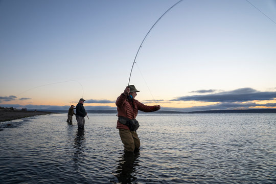 Two fly fishermen cast for searun coastal cutthroat trout and salmon with their guide standing between them on a salt water beach  on a beach on the west coast of the USA