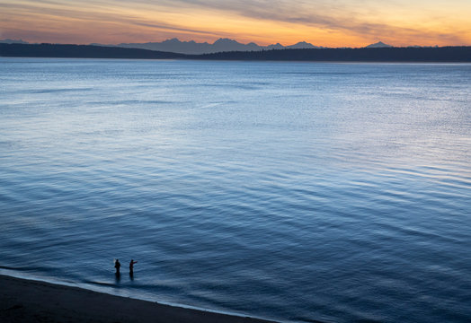 A view from above of a guide and a fly fisherman at the water's edge, fishing for salmon and sea run coastal cutthroat trout at a beach on the north west coastline of the USA.  