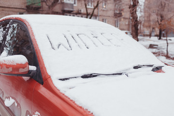 White snow lies on the car with the inscription Winter
