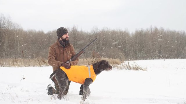 young ambitious man and his dog sitting on the snow. hunter resting with a pet outdoors