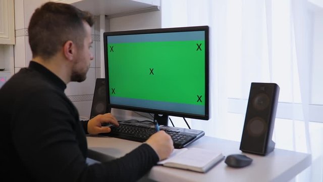 Man using PC computer with green screen chroma key at home rewrite information into notebook