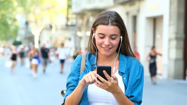 Front view of a girl choosing and listening to music from smart phone outdoor in the street
