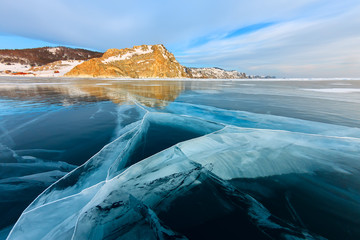 the cross of deep cracks in the thick ice of the winter lake Baikal opposite the rocky mountain of...