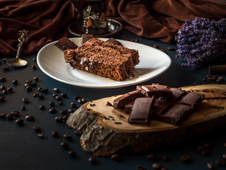 Arrangement of slice chocolate cake and pieces of coffee and chocolate on dark background. Chocolate brownie served with pieces of chocolate. Holiday arrangement. 