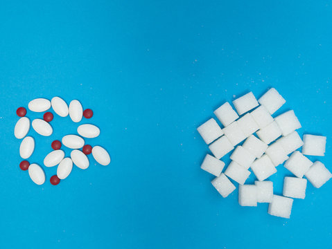 sugar substitute pills like stevia or aspartame and white blocks of refined sugar on blue background. flat lay from the top image