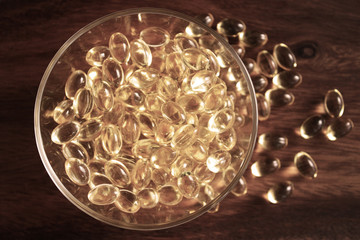 Transparent yellow pills in bowl on wood background. Capsules cod liver oil, omega 3. Advertising Healthy lifestyle, possibility of addiction to medication and excess dosage.