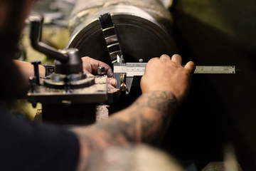 Cropped tattooed man taking the measure of the piece on the lathe