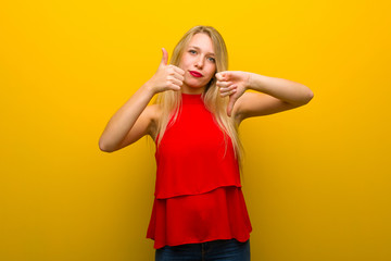 Young girl with red dress over yellow wall making good-bad sign. Undecided between yes or not