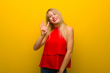 Young girl with red dress over yellow wall happy and counting four with fingers