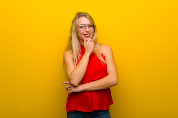 Young girl with red dress over yellow wall with glasses and smiling