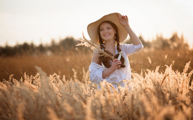 Fototapeta na wymiar Portrait of a fair-haired young girl in a hat, summer evening in the field