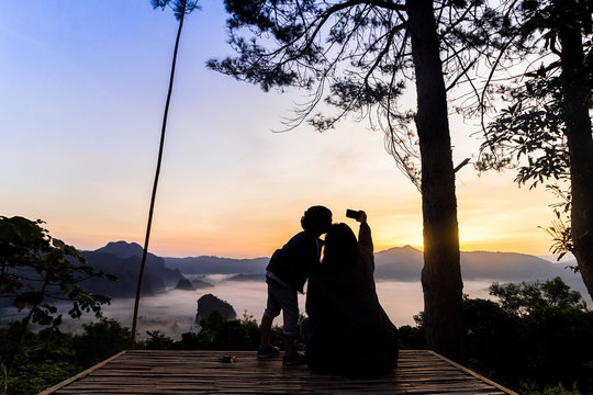 The silhouette of Mother and child are taking photos up on the cliffs and watch the misty valley at the sunrise.