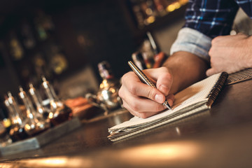 Young bartender standing at bar counter taking notes close-up