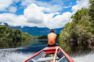 close up view from behind of young bare chested indigenous man with riding wooden boat in jungle...