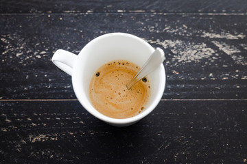 cup of coffee with foam and spoon from above on dark wood