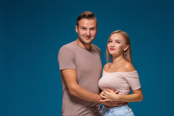 Young couple is hugging on blue background in studio. They wear T-shirts, jeans and smile.