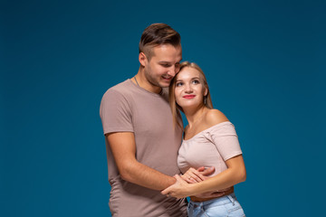 Naklejka premium Young couple is hugging on blue background in studio. They wear T-shirts, jeans and smile.