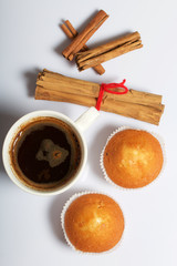 A cup of freshly brewed coffee and muffins. Nearby are cinnamon sticks. On a white background.