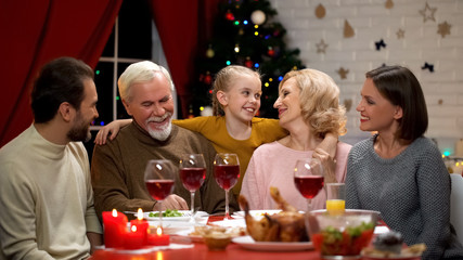 Happy adorable girl hugging grandparents, family having traditional Xmas dinner