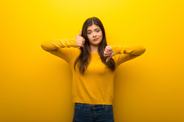 Teenager girl on vibrant yellow background making good-bad sign. Undecided between yes or not
