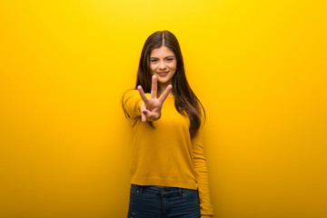 Teenager girl on vibrant yellow background happy and counting three with fingers
