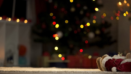 Fototapeta na wymiar Teddy bear toy lying near Christmas tree, forgotten winter holidays in orphanage