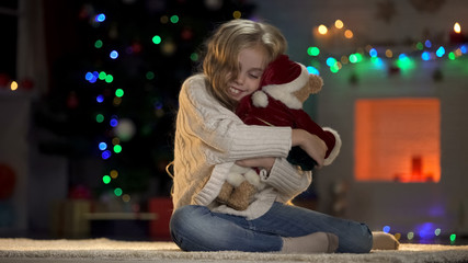 Happy girl hugging teddy bear in Santa costume, belief in X-mas fairy-tale