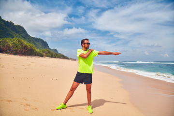 Sportsman stretching on a exotic tropical beach after jogging / exercising.