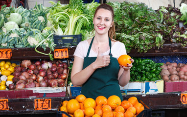Seller female is holding oranges on her workplace in the market.