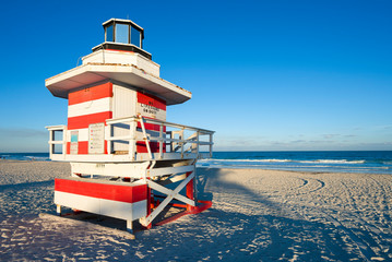 Fototapeta premium Scenic afternoon view of a classic wooden lifeguard tower painted in red and white stripes with sunset shadows in South Beach, Miami, Florida, USA