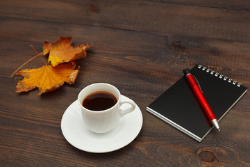 Cup of espresso, black notebook, pen and autumn yellow leaf on a wooden background