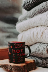 Folding knitted woolen sweaters, a stack of old books, a beautiful black and red cup on a cozy fluffy beige blanket.