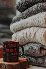 Folding knitted woolen sweaters, a stack of old books, a beautiful black and red cup on a cozy fluffy beige blanket.