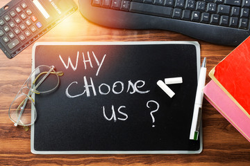 why choose us ? question writing with white chalk on blackboard and keyboard, books and calculator,...