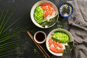 Bowl with Hawaiian salmon poke , rice, avocado and nori on a dark stone background with palm branch .Sushi bowl. Top view, copy space.