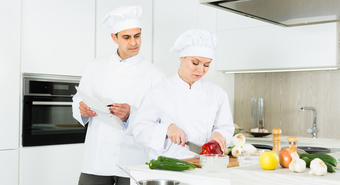 Woman and man professionals are cooking salad in the kitchen
