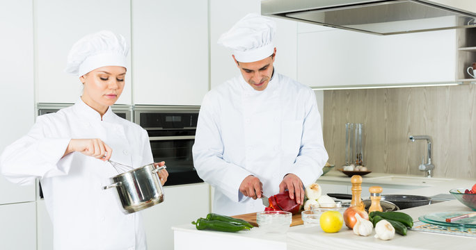 Professional chefs  in uniform  working with vegetables on kitchen