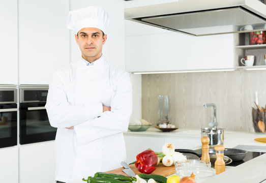 Male chef  in white uniform standing near workplace on kitchen