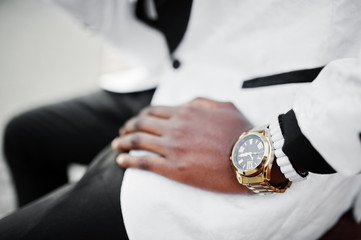 Chic handsome african american man in white suit sitting on bench. Close up photo of golden watches...
