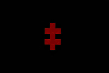Fototapeta premium Red puzzle piece or two-barred cross isolated on black background