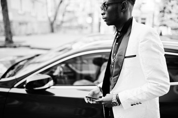 Chic handsome african american man in white suit against red luxury car with mobile phone at hand.