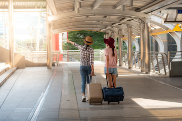 The back of two teenage girls who are friends, walking in the street or the walkway, holding carrying a suitcase, trolley wheel. To summer and travel concept.