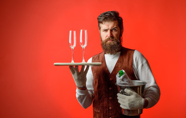 Waiter in uniform serving wine glasses. Waiter holds ice bucket with champagne bottle&tray with glasses. Butler with wine cooler with bottle of champagne&tray with glass. Professional catering service