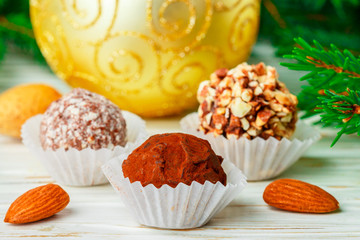 Homemade chocolate truffles with almonds, coconut and biscuits crumb in a white plate on the table with fir branches and festive toys balls. Gift for Christmas and New year. Gourmet. Selective focus