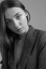 Black and white portrait of pretty woman professional model without make up, thick eyebrows, oval face, parting in the middle, long dark hair, wearing classy jacket
