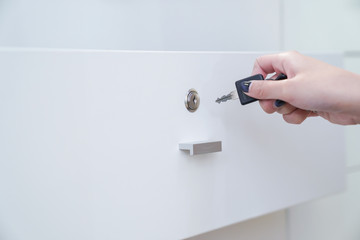 women hand holding the black simple key to open the white wardrobe. Clear background.