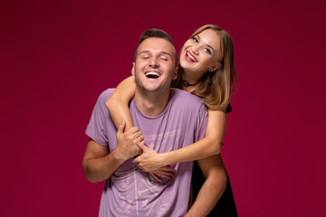 Young nice couple posing in the studio, express emotions and gestures, smiling, on a burgundy background