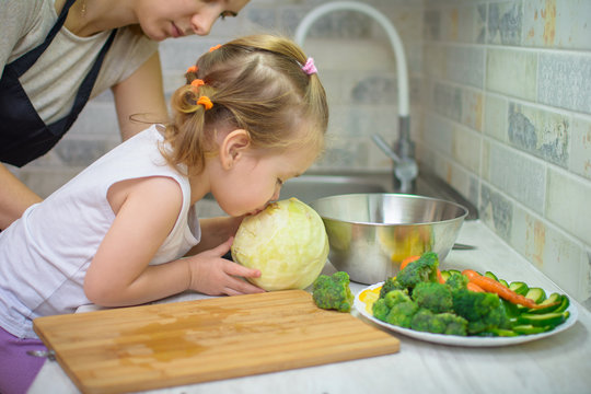happy young woman with little daughter cooking with vegetables at home kitchen. Healthy eating concept. Vegan food
