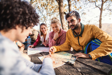 Hikers sitting on the bench at the table in the woods and looking at map. Autumn season.